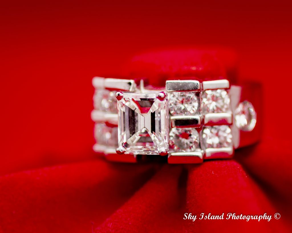 Women's diamond engagement ring on a red setting with five diamonds on each side of center emerald cut diamond. Sky Island photography John Heyward